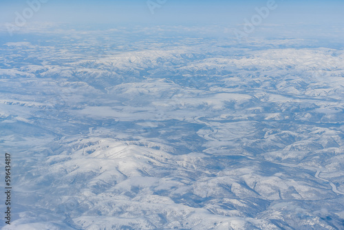 Aerial view of a winding river among high hills and mountains in the tundra. Siberia, Far East of Russia. Snow-covered tundra in the Arctic.