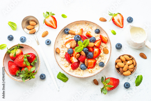 Oatmeal porrige with fresh berries and nuts on white background. Healthy breakfast, top view with copy space.