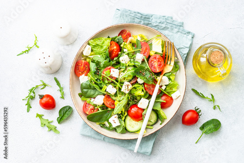 Spring salad in craft plate. Spinach, arugula, tomatoes and feta with olive oil. Top view on white.