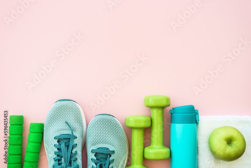 Fitness equipment on pink background, flat lay image. Sneakers, dumbbells, towel and bottle of water. Training, workout and fitness concept.