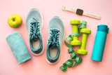 Healthy lifestyle and fitness concept. Sneakers, dumbbells, towel, green apple and fitness bracelet. Flat lay on pink.