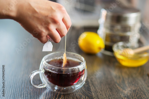 Woman puts the tea bag in the glass cup with hot water