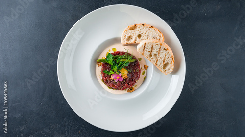 Appetizer of beef tartare with egg, greens, fried bread slices and sauce.