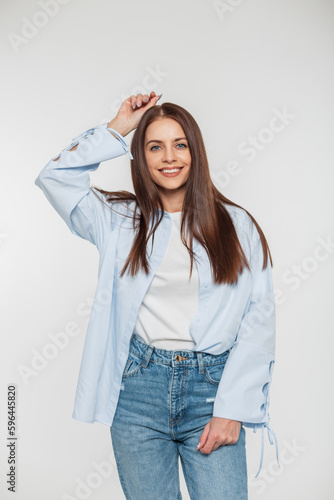 Happy young model woman with a smile with long hair in fashionable denim casual clothes with a shirt stands on a white background