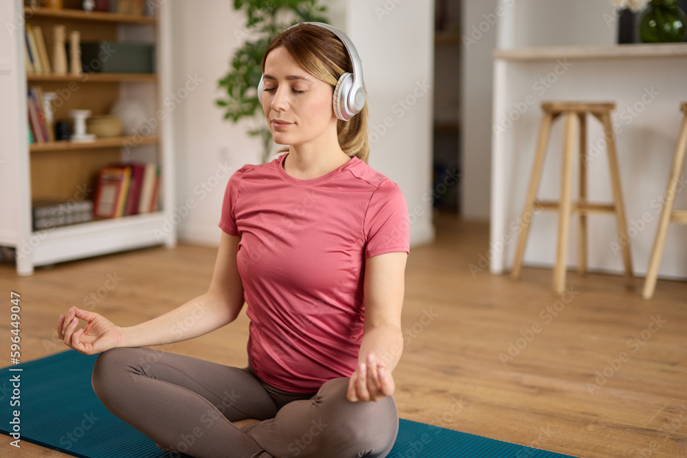 Beautiful young woman with headphones meditating on yoga mat at home Beautiful young woman with headphones meditating on yoga mat at home