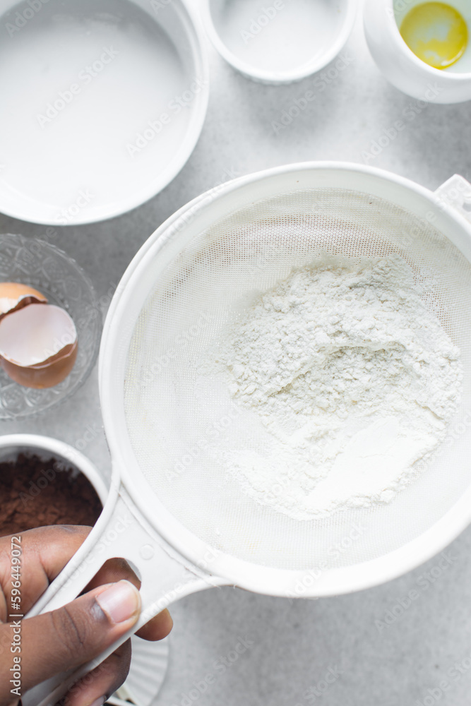 All purpose flour in a white sieve, sifting baking flour into a large bowl All purpose flour in a white sieve, sifting baking flour into a large bowl