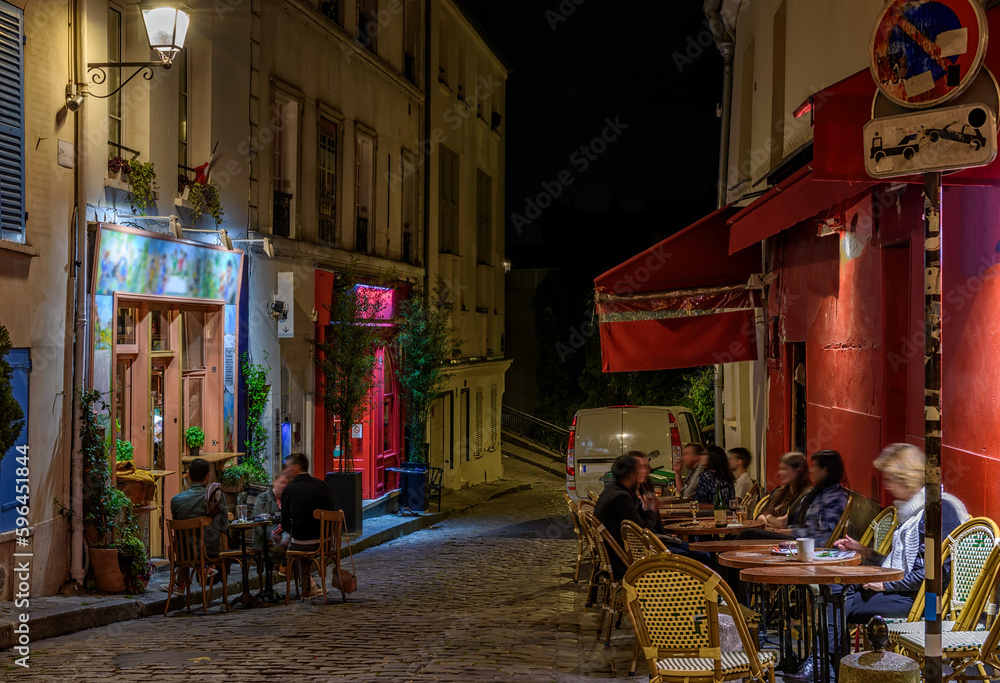 Night cozy street with tables of cafe in quarter Montmartre in Paris, France. Architecture and landmark of Paris. Paris cityscape.