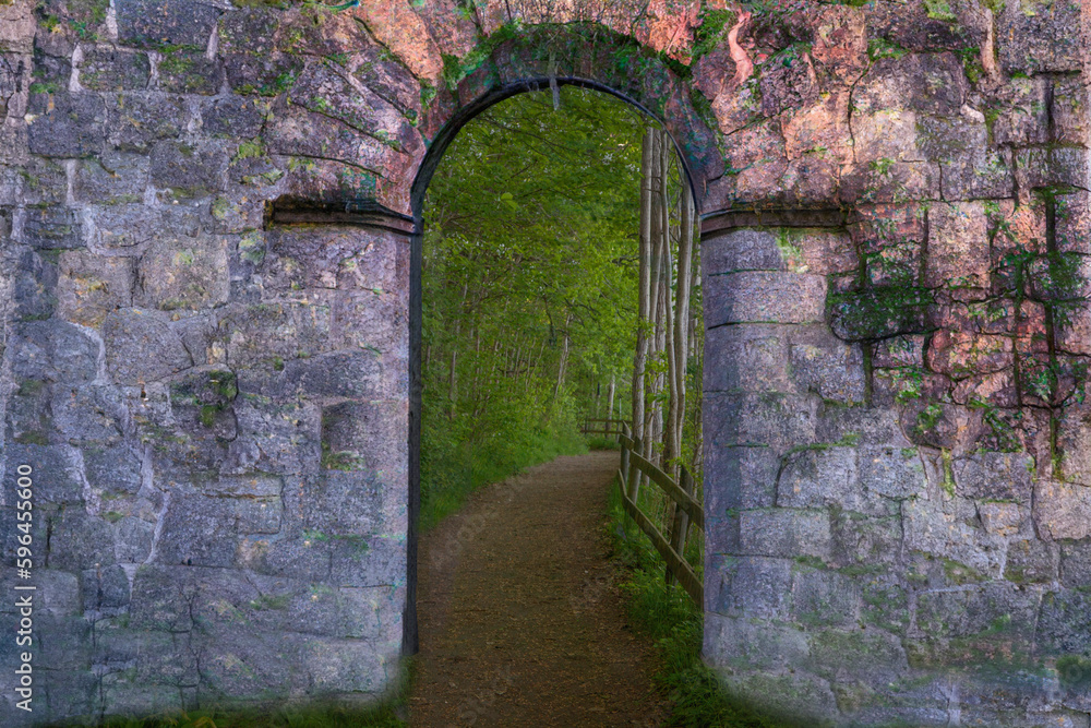 Gate in old wall. On the outside of the wall we see a path that goes through a dense forest