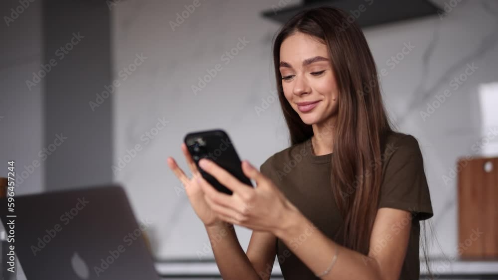 Young woman working on laptop and typing at phone in the kitchen Young woman working on laptop and typing at phone in the kitchen