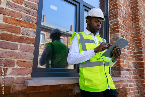 Φωτογραφία Handsome african american architect in reflective vest and white helmet working on digital tablet near construction site