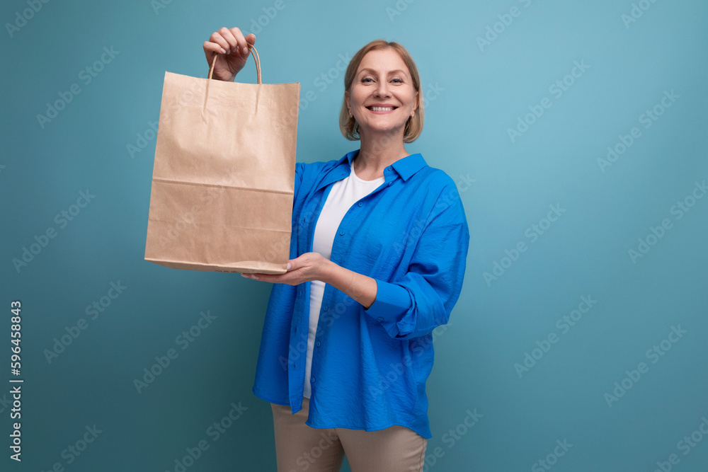 happy mature woman holding craft bag for shopping on blue background copy space happy mature woman holding craft bag for shopping on blue background copy space