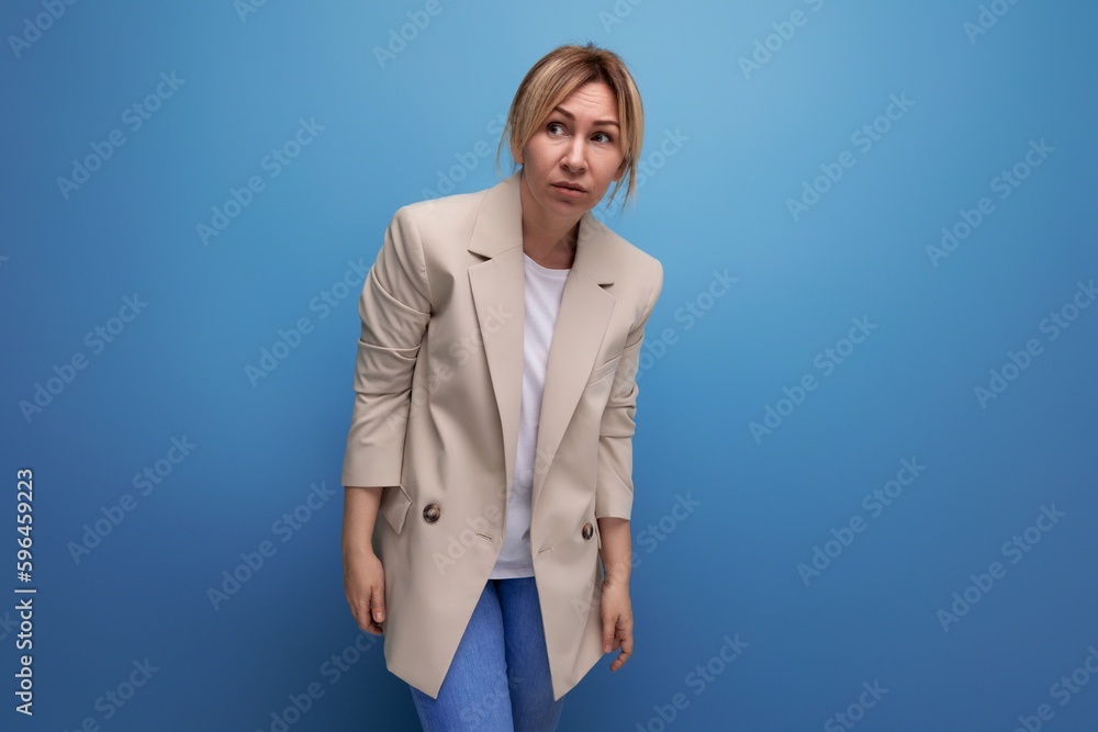 portrait of a pretty blond millennial woman in a cream-colored jacket posing on a blue background copy space portrait of a pretty blond millennial woman in a cream-colored jacket posing on a blue background copy space