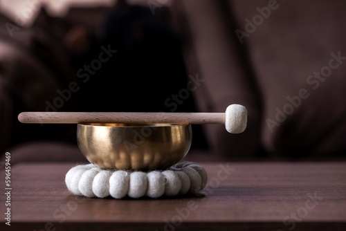 A close up of a himalayan bowl or tibetan singing bowl, with a mallet lying on top of it to make a relaxing sound. The object is used for therapy to relieve stress and meditation, relaxation.