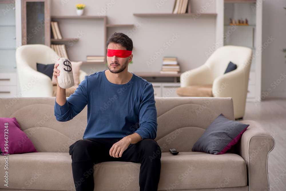 Young blindfolded man holding moneybag at home Young blindfolded man holding moneybag at home