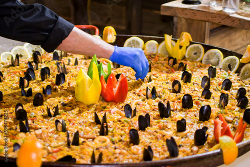 Chef working in the restaurant kitchen preparing a large seafood paella with vegetables, fruits and mussels
