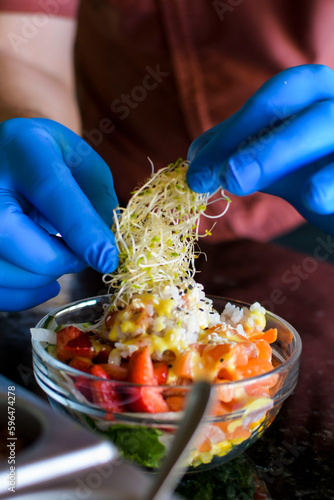 Hands of man doing food styling with blue gloves setting up plate of poke salad in a bowl