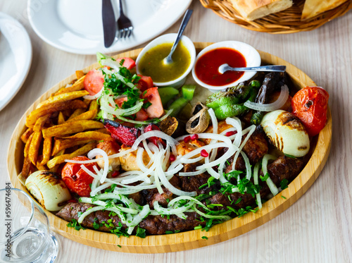 Dish with a appetizing assorty of Georgian cuisine of delicious shish kebab, french fries, baked vegetables, mushrooms,..peppers, fresh tomatoes, tkemali sauce, pita bread and sprinkled with chopped photo