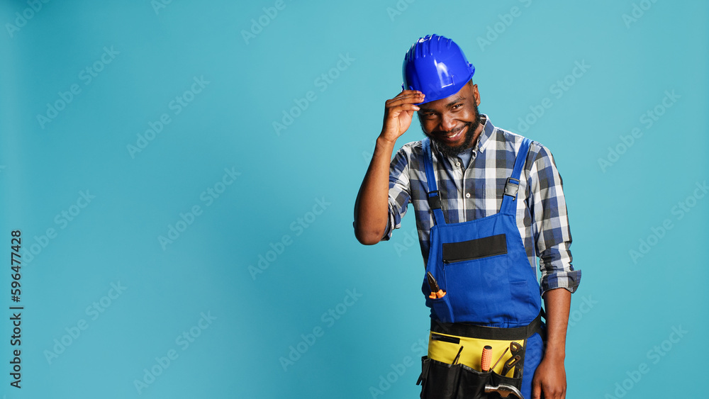 Fototapeta premium African american craftsman being humble saying hello, acting positive and smiling in studio. Young cheerful putting hat down and showing respect on camera, building carpentry profession.