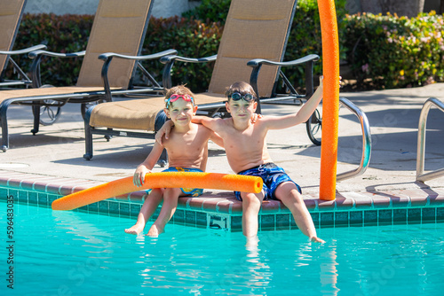 Oudoor summer activity. Concept of fun, health and vacation. Brothers boys eight and five years old in swim glasses with noodles sits and laught near a pool in hot summer day.