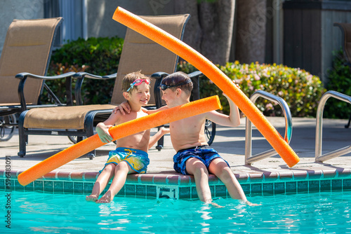 Oudoor summer activity. Concept of fun, health and vacation. Brothers boys eight and five years old in swim glasses with noodles sits and laught near a pool in hot summer day.