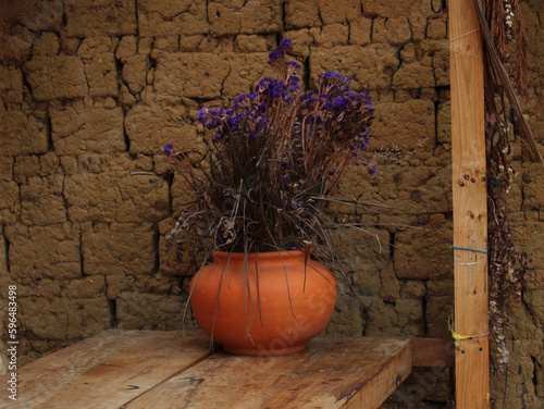 Jarrón de barro artesanal con flores moradas sobre una mesa de madera © AnaSofia