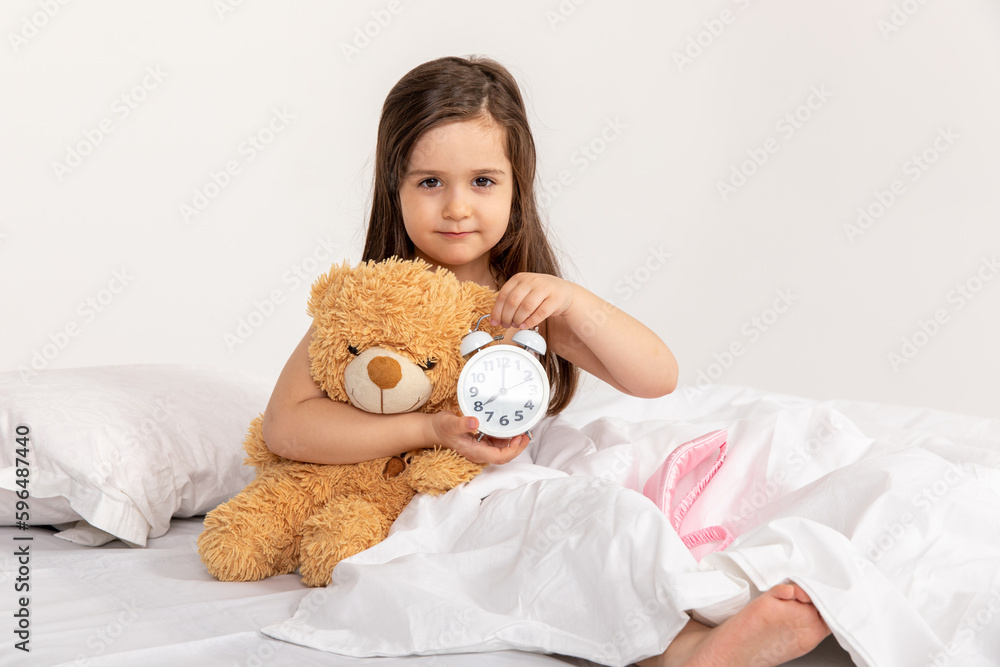 happy little blonde girl in a white bed with an alarm clock, good morning happy little blonde girl in a white bed with an alarm clock, good morning