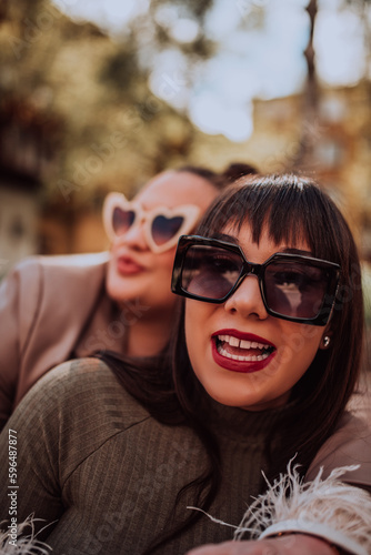 Two young women embrace each other emotionally outside on a sunny day while wearing sunglasses