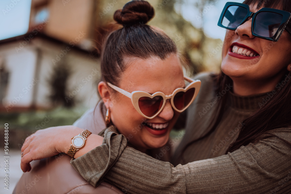 Two young women embrace each other emotionally outside on a sunny day while wearing sunglasses