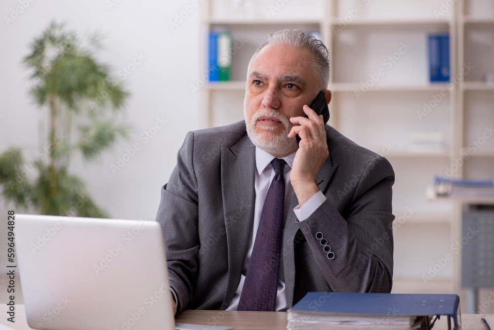 Old male employee speaking by phone at workplace Old male employee speaking by phone at workplace