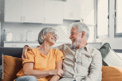 Happy laughing older married couple talking, laughing, standing in home interior together, hugging with love, enjoying close relationships, trust, support, care, feeling joy, tenderness.