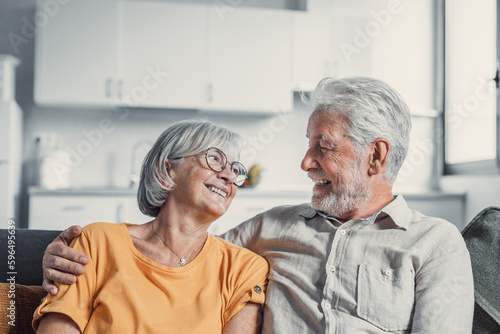 Happy mature husband and wife sit rest on couch at home hugging and cuddling, show care affection, smiling senior loving couple relax on sofa have fun, enjoy tender romantic family weekend together.