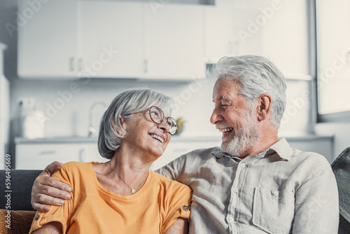 Happy mature husband and wife sit rest on couch at home hugging and cuddling, show care affection, smiling senior loving couple relax on sofa have fun, enjoy tender romantic family weekend together.