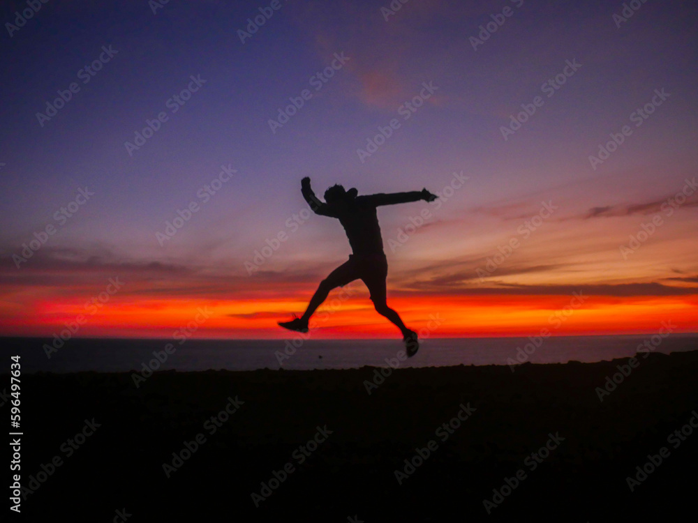 The thrill of adventure with the silhouette of a man jumping near a cliff in front of the ocean at sunset