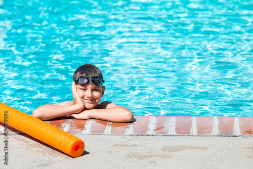 Oudoor summer activity. Concept of fun, health and vacation. A happy boy eight years old in swimming goggles is holding onto the side of the pool on a hot summer day.