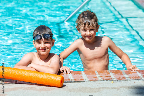 Oudoor summer activity. Concept of fun, health and vacation. A happy brothers boys eight and five years old in swimming goggles are holding onto the side of the pool on a hot summer day.