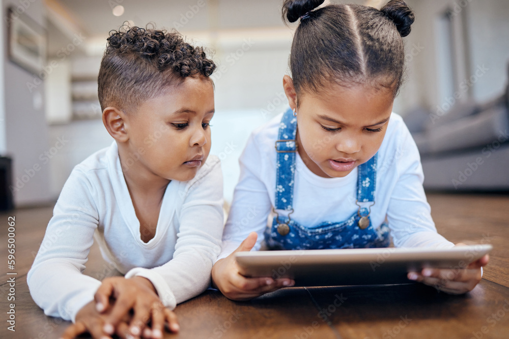 Two young mixed race children using a digital tablet while lying together on the floor at home. Young boy and girl siblings browsing the internet online to play games and learn from educational apps Two young mixed race children using a digital tablet while lying together on the floor at home. Young boy and girl siblings browsing the internet online to play games and learn from educational apps
