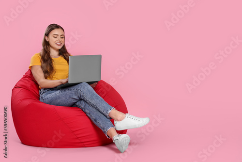 Foto Happy woman with laptop sitting on beanbag chair against pink background
