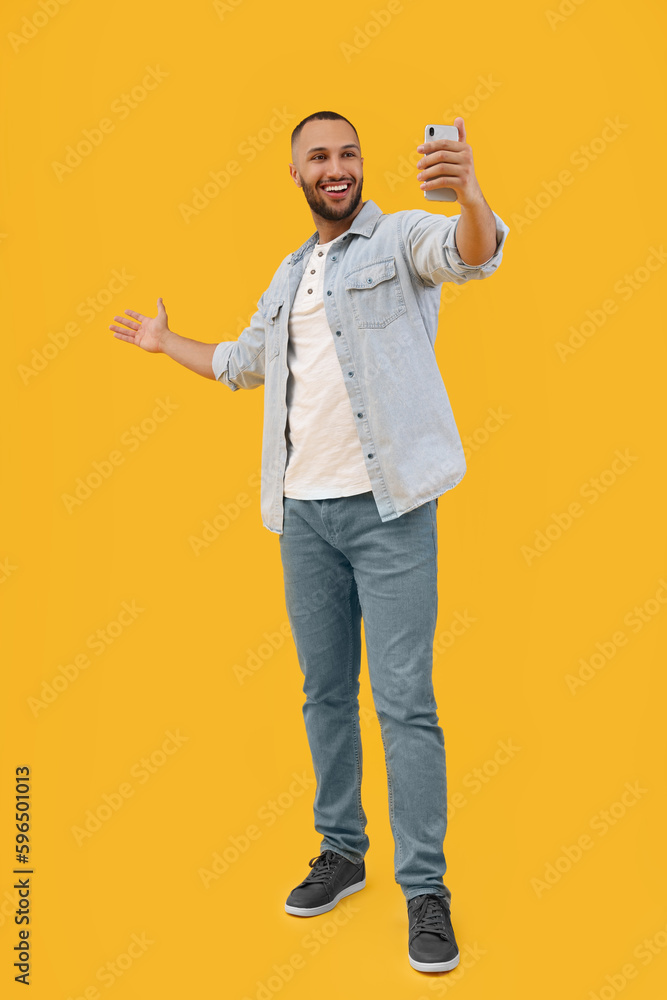 Smiling young man taking selfie with smartphone on yellow background Smiling young man taking selfie with smartphone on yellow background