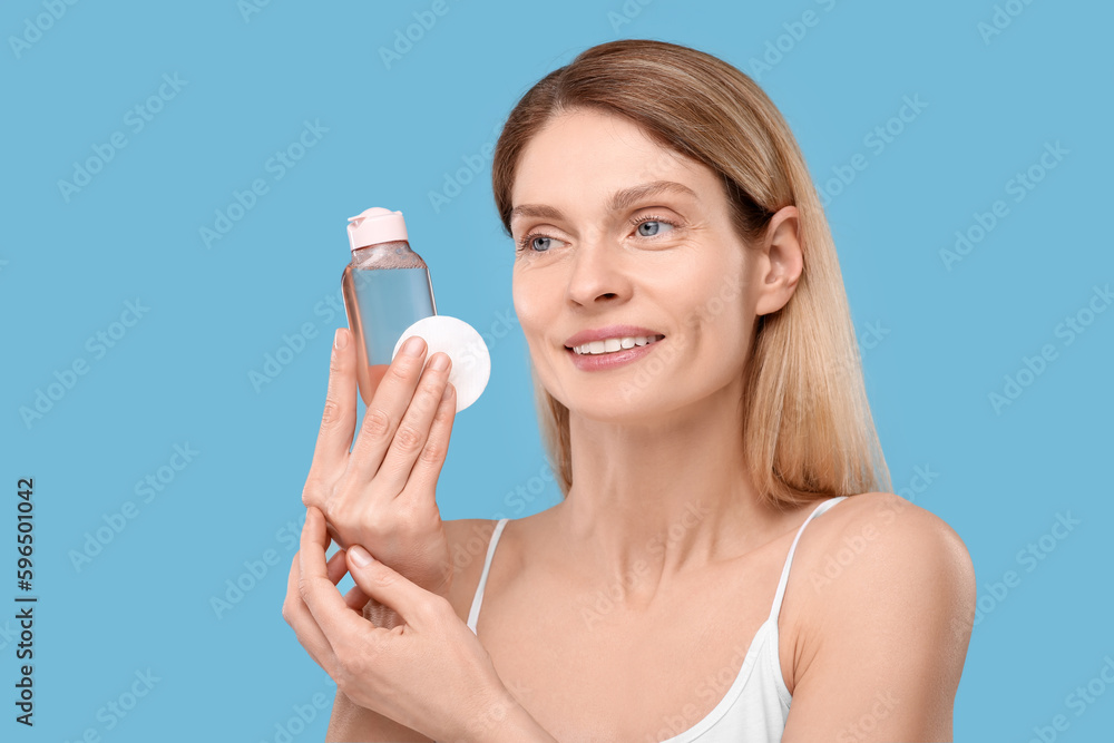 Beautiful woman with makeup remover and cotton pad on light blue background Beautiful woman with makeup remover and cotton pad on light blue background