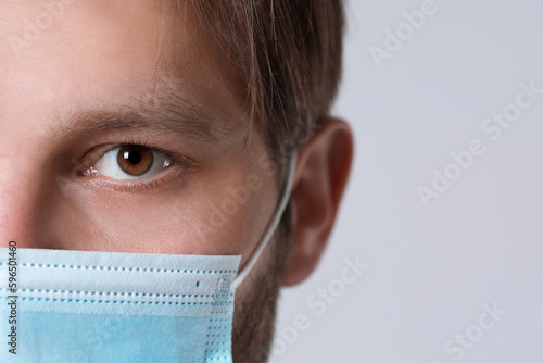 Doctor or medical assistant (male nurse) with protective mask on light grey background, closeup. Space for text photo