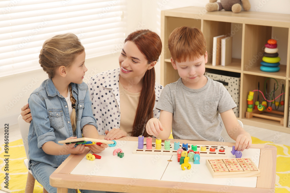 Happy mother and children playing with different math game kits at desk in room. Study mathematics with pleasure Happy mother and children playing with different math game kits at desk in room. Study mathematics with pleasure