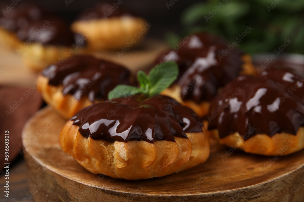 Delicious profiteroles with chocolate spread and mint on wooden board, closeup Delicious profiteroles with chocolate spread and mint on wooden board, closeup