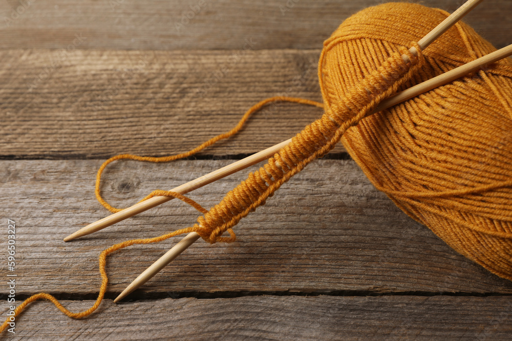 Soft orange yarn, knitting and needles on wooden table, closeup Soft orange yarn, knitting and needles on wooden table, closeup