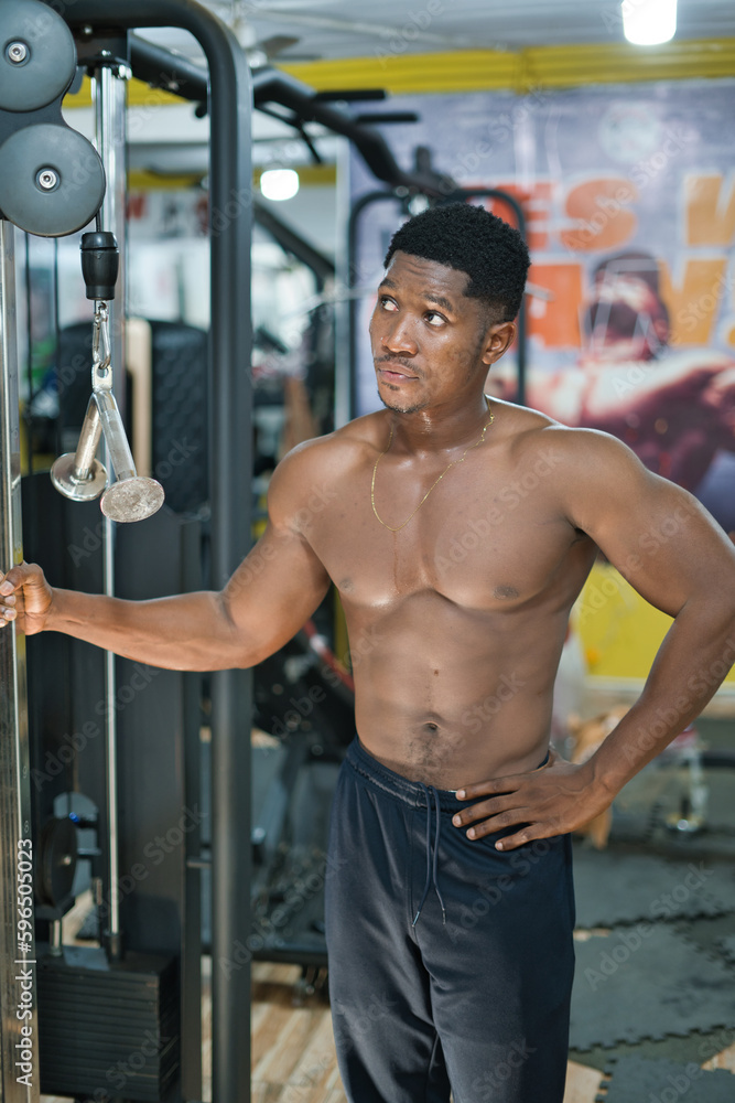 A young black male exercises in a gym, building physical strength and vitality through weight training for sports performance.