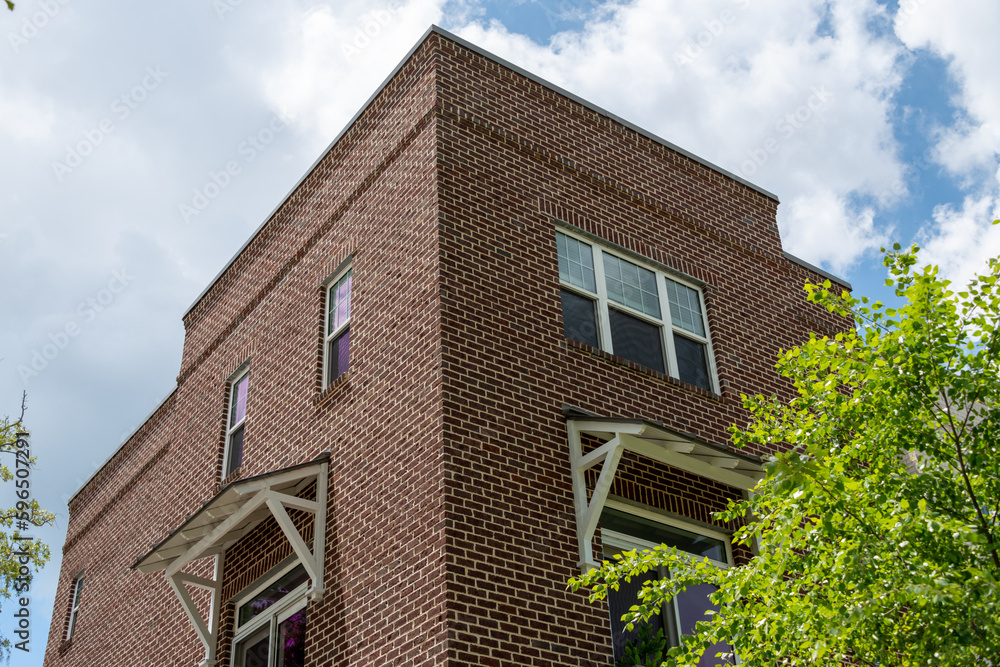 The exterior of a tall brown colored brick building with multiple double hung windows with white trim. The vintage apartment building has a canopy over the lower floor windows to shade the interior. 