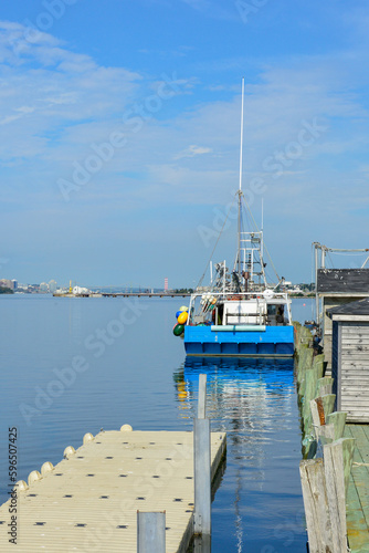 A vibrant blue colored fishing boat docked at a wooden port. The boat has markers, buoys, trackers, and nets on the back of the vessel. The industrial boat is moored in Halifax Harbour, Canada.  photo