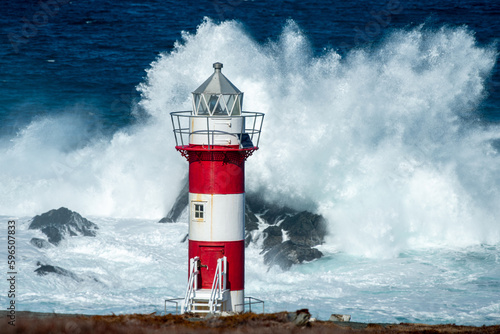 Fotografia A tall circular lighthouse tower has horizontal red and white colors against a stormy sea