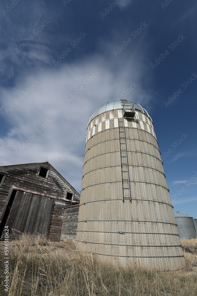 Cement grain seed silo next to abandoned wooden barn