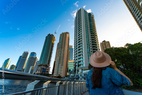 back view of a long hair woman in a hat watching the sunset over brisbane city  city reach boardwalk with amazing view of large skyscrapers by brisbane river  australia