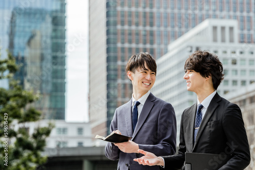 ビジネス街を歩きながら会話の弾む20代と30代の上司と部下の2人の男性ビジネスマン